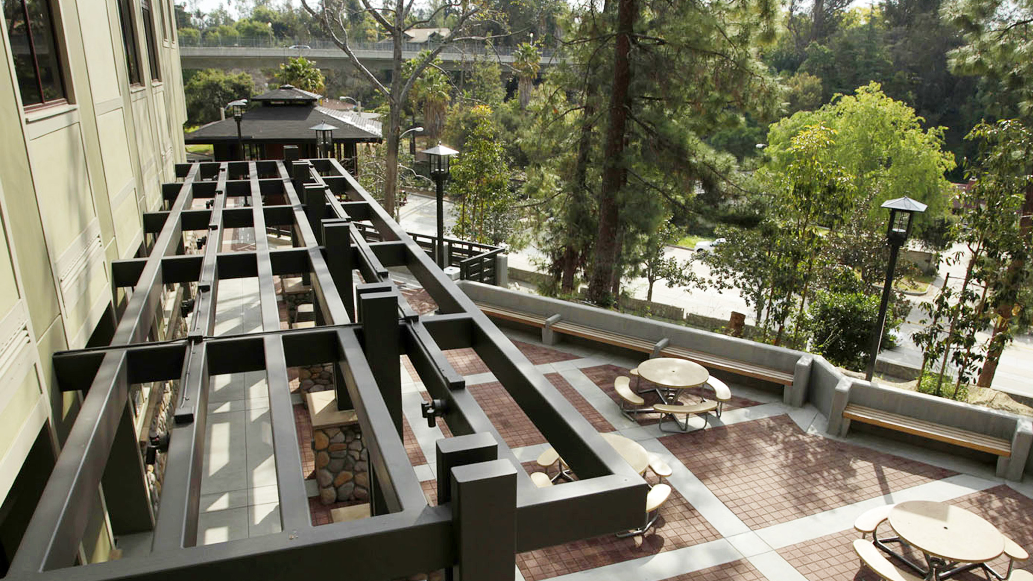 High-angle view of a terrace with round lunch tables and attached benches at the new middle school at the Chandler School in Pasadena, an educational architecture project in Southern California, as seen through the decorative wooden overhang.