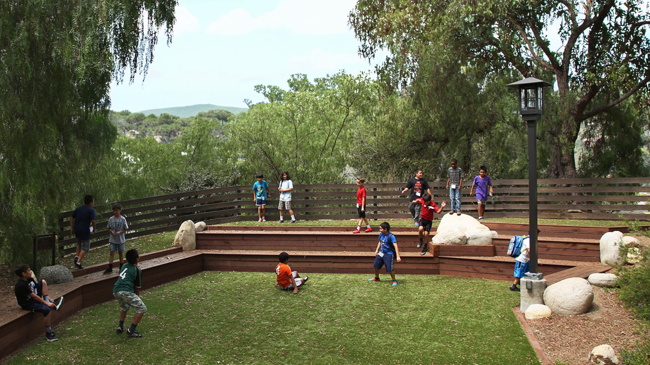 Students play in a grassy area with terraced wooden structures at the Chandler School in Pasadena, an educational architecture project in Southern California.