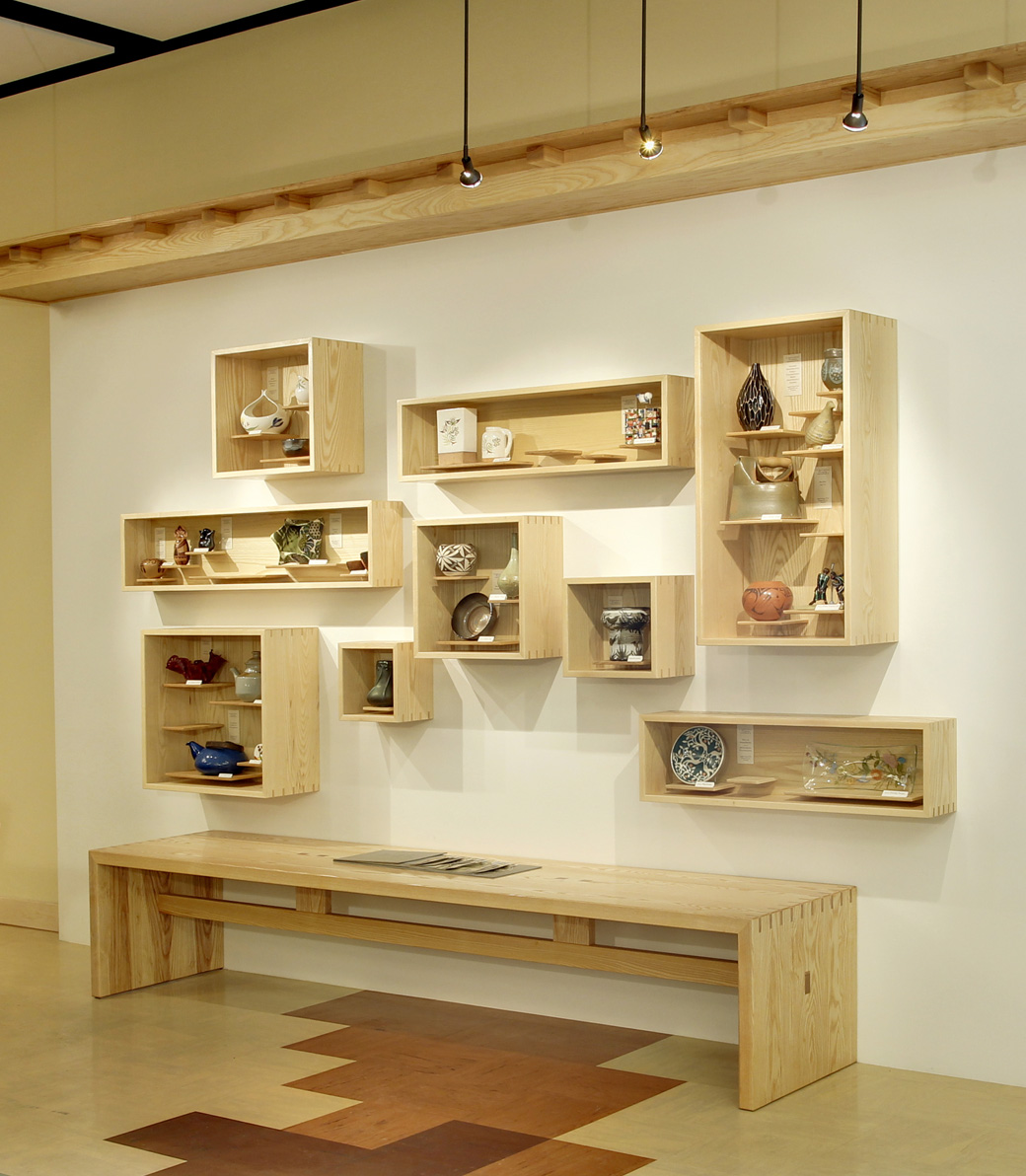 A set of wall-mounted, open display cabinets filled with ceramics in the Downtown Women's Center in Los Angeles, a Pica+Sullivan Southern California non-profit architectural renovation project, from a low angle, focusing on the windows and decorative features.