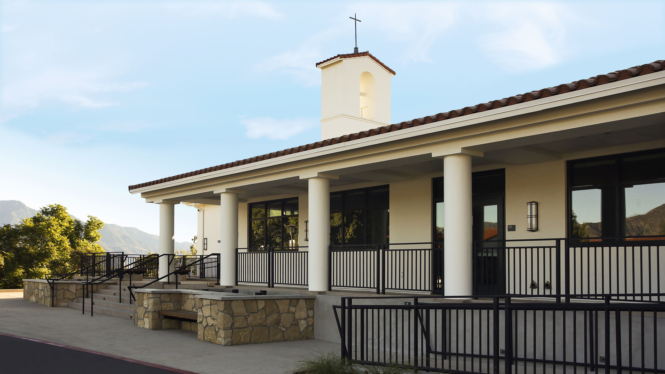 The front entrance of the Mozilo Family Center for the Arts at the Flintridge Sacred Arts Academy, an educational architectural project in Southern California. A tower with a cross topping it is visible at the front end of the building.