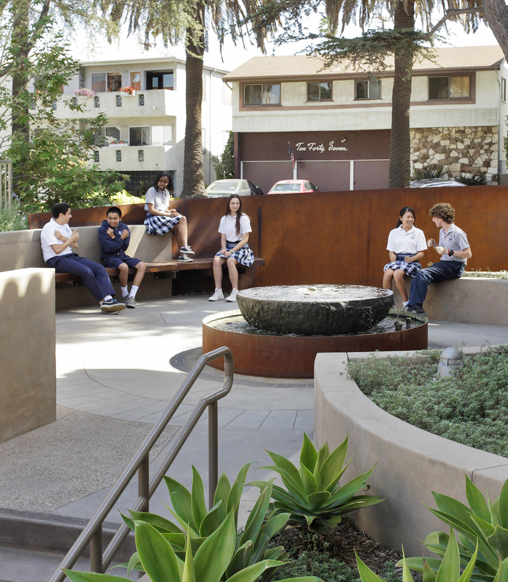 Students talk in an exterior plaza with benches at the Saint Monica Community Center in Santa Monica, a Pica+Sullivan Southern California educational and religious architectural project.