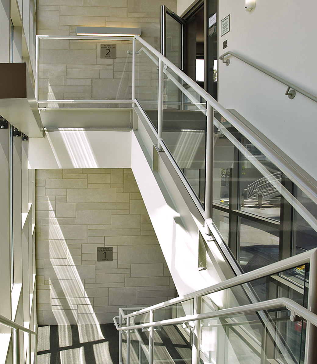 The staircase from first floor to the second floor, with light streaming in from the wall of windows, at the Saint Monica Community Center in Santa Monica, a Southern California religious and educational architectural project.