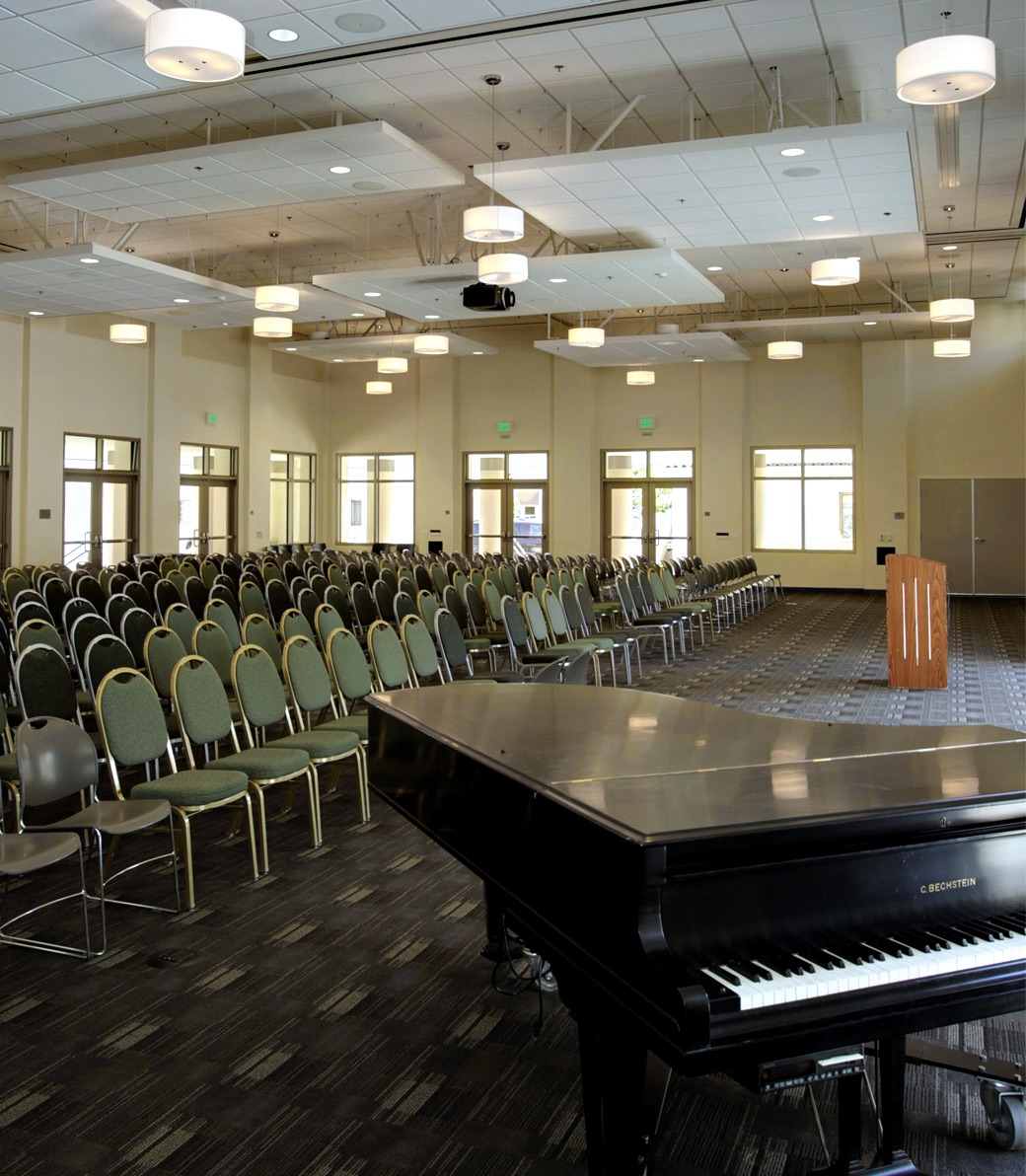 An assembly room with a piano and rows of empty chairs facing a lectern at the Saint Monica Community Center in Santa Monica, a Southern California religious architectural project.