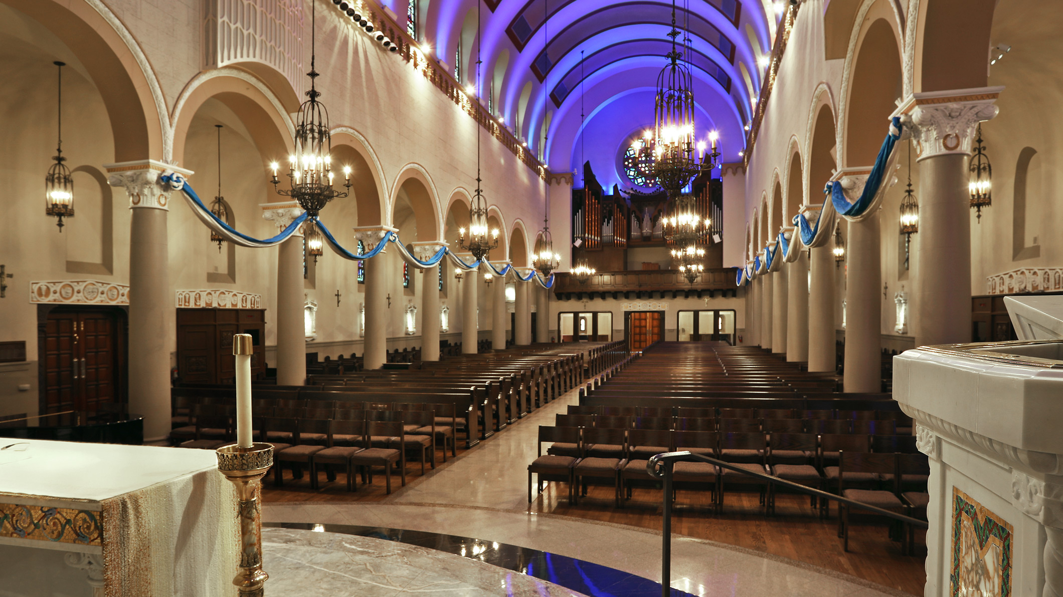 View of the empty pews from the altar at Saint Monica Church in Santa Monica, a Pica+Sullivan Southern California religious architectural renovation project. The ceiling is lit in purple.