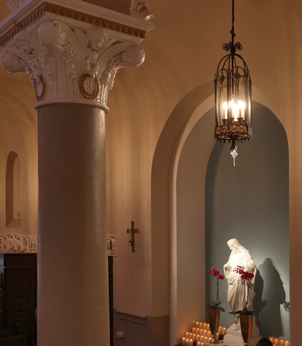 An alcove with a marble statue of Jesus Christ with devotional candles at Saint Monica Church in Santa Monica, a Pica+Sullivan Southern California religious architectural renovation project.