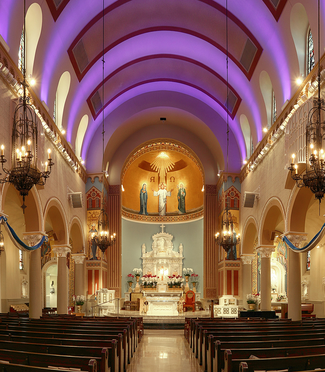 Saint Monica Church in Santa Monica, a Pica+Sullivan Southern California religious architectural renovation project, with a marble statue, devotional candles, and confessionals in the background. The altar is centered, facing the empty pews, and purple lighting illuminates the ceiling above.