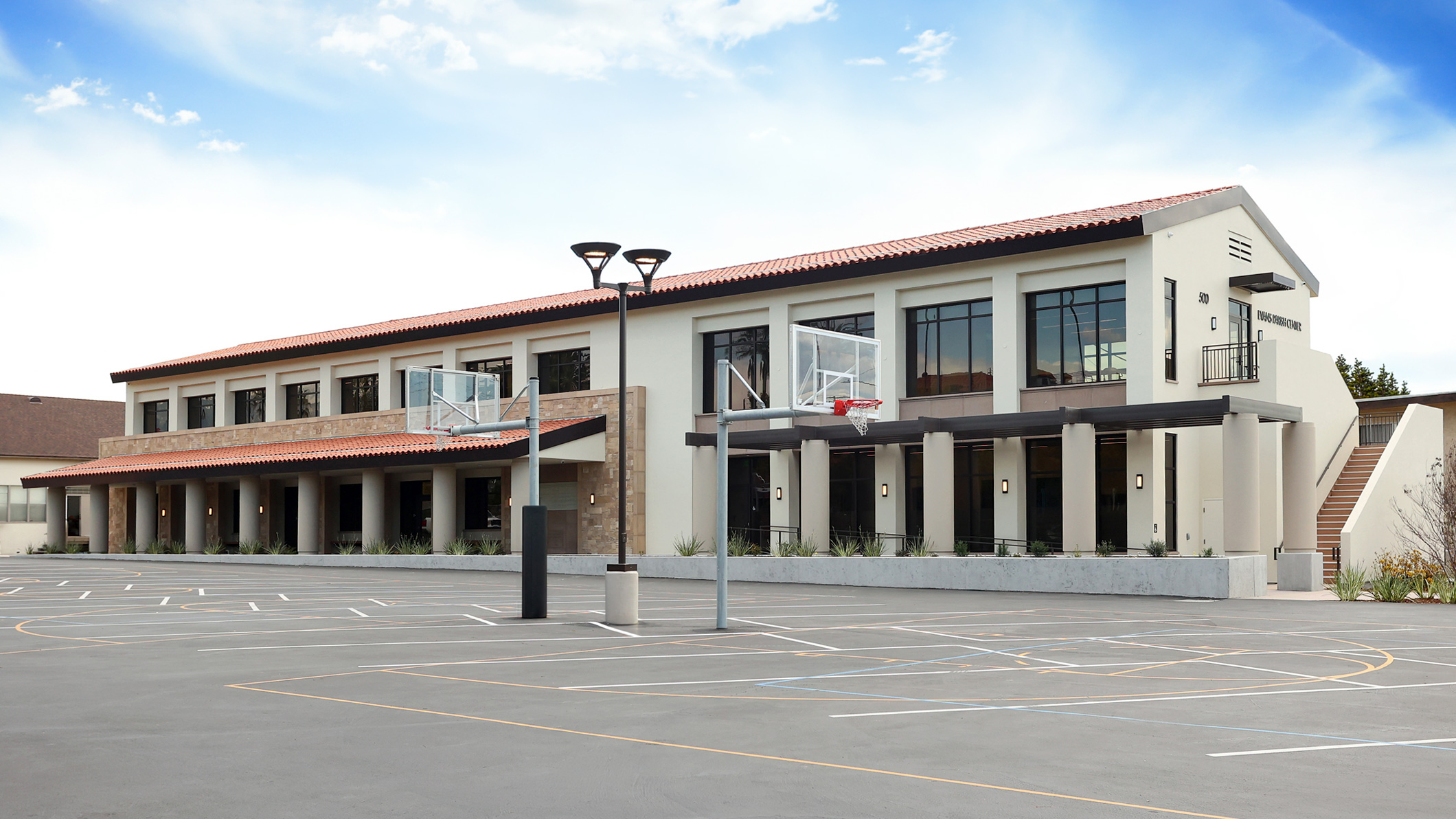Parking lot and exterior basketball court at the Holy Family Church Parish Center in Glendale, a Pica+Sullivan Southern California religious architectural project, with a focus on the columns and porch overhang.