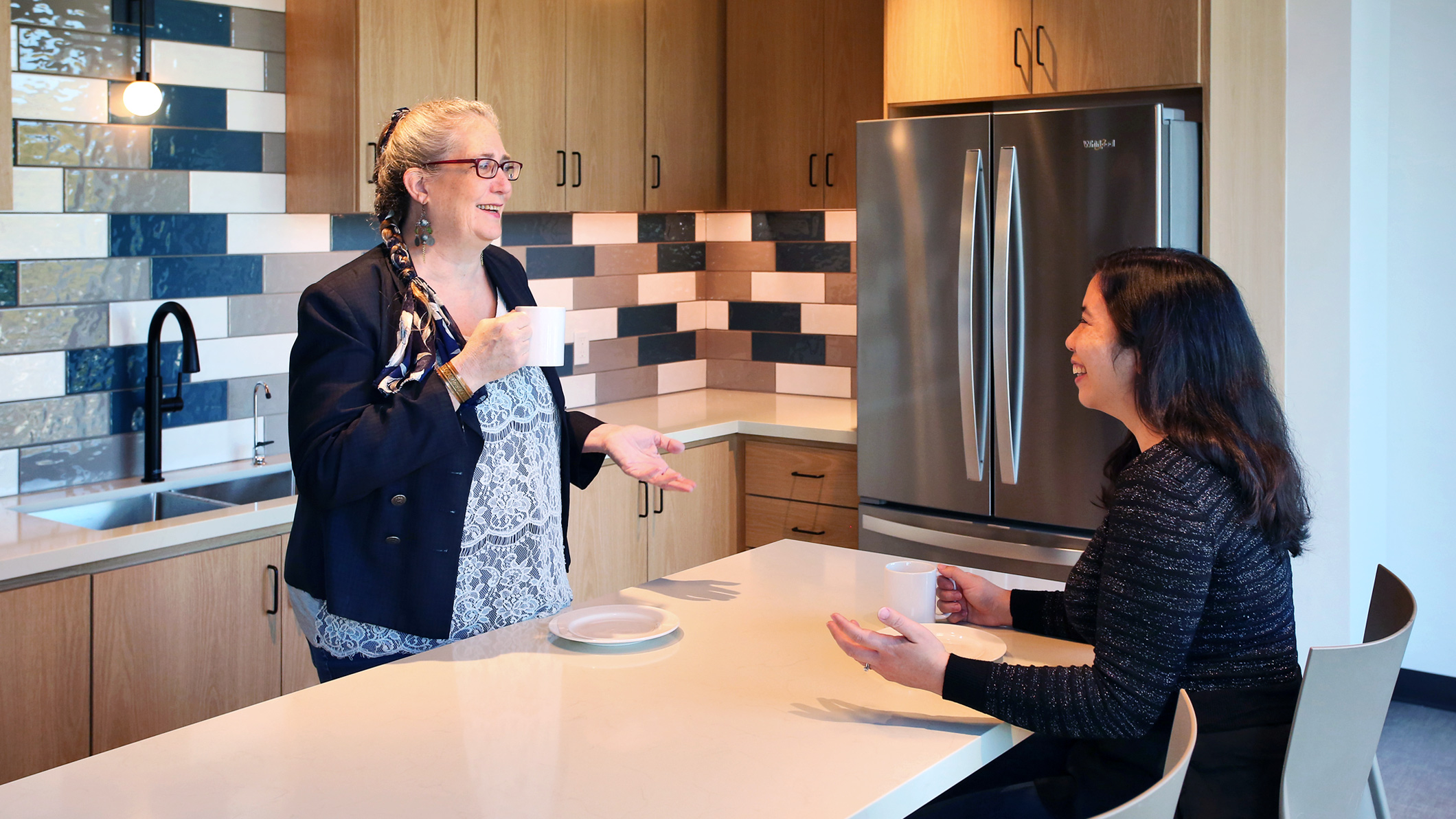 Two women talk over coffee in akitchen at the Holy Family Church Parish Center in Glendale, a Pica+Sullivan Southern California religious architectural project.