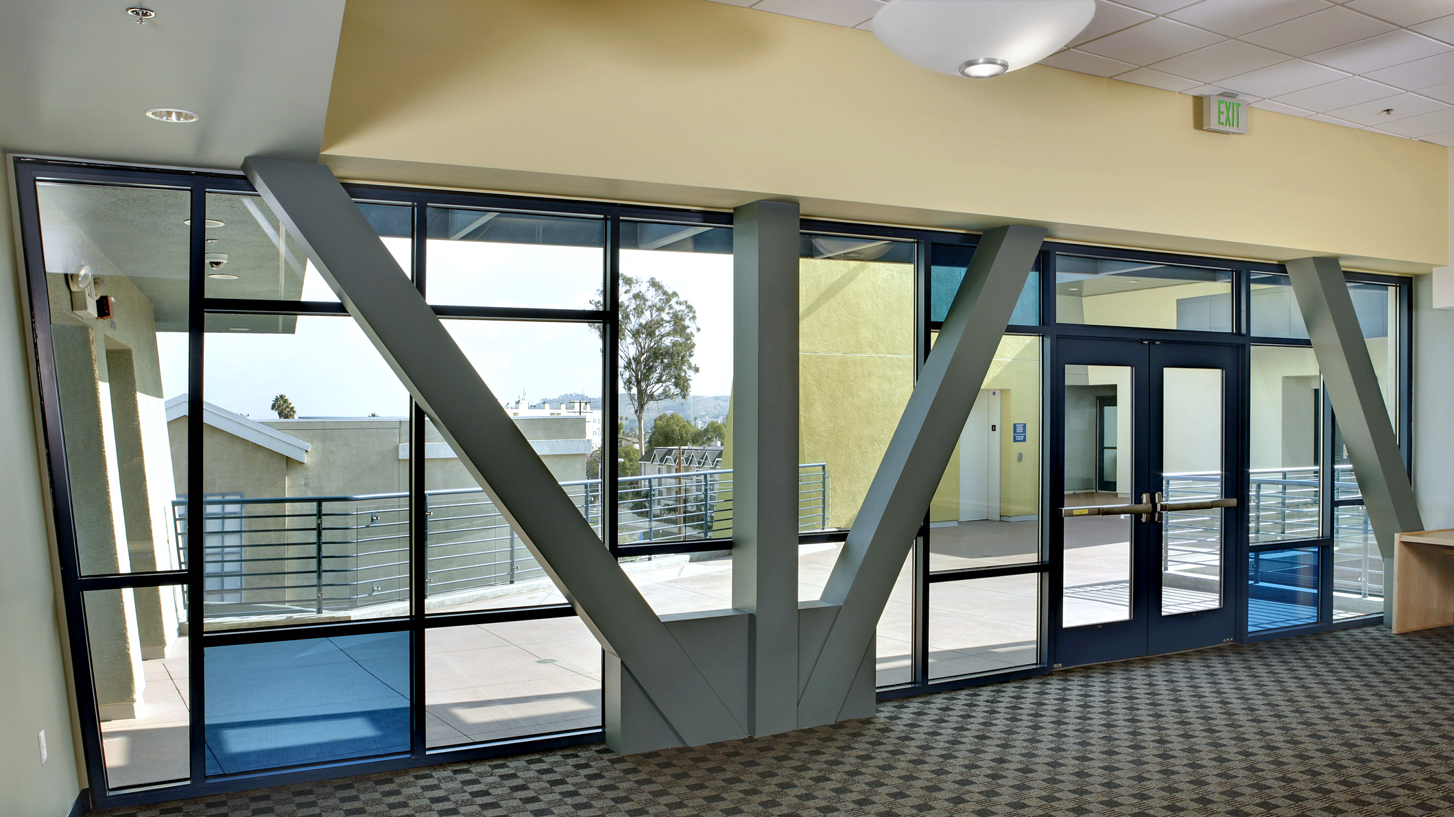 A hallway with a wall of glass windows looking out onto a second-floor landing at Le Français de Los Angeles in Los Angeles, a Pica+Sullivan Southern California educational architectural project.