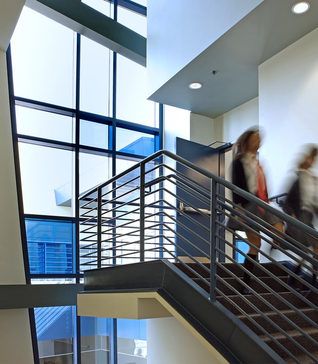 Students walk down an interior staircase in front of a large wall of windows at Le Français de Los Angeles in Los Angeles, a Pica+Sullivan Southern California educational architectural project.