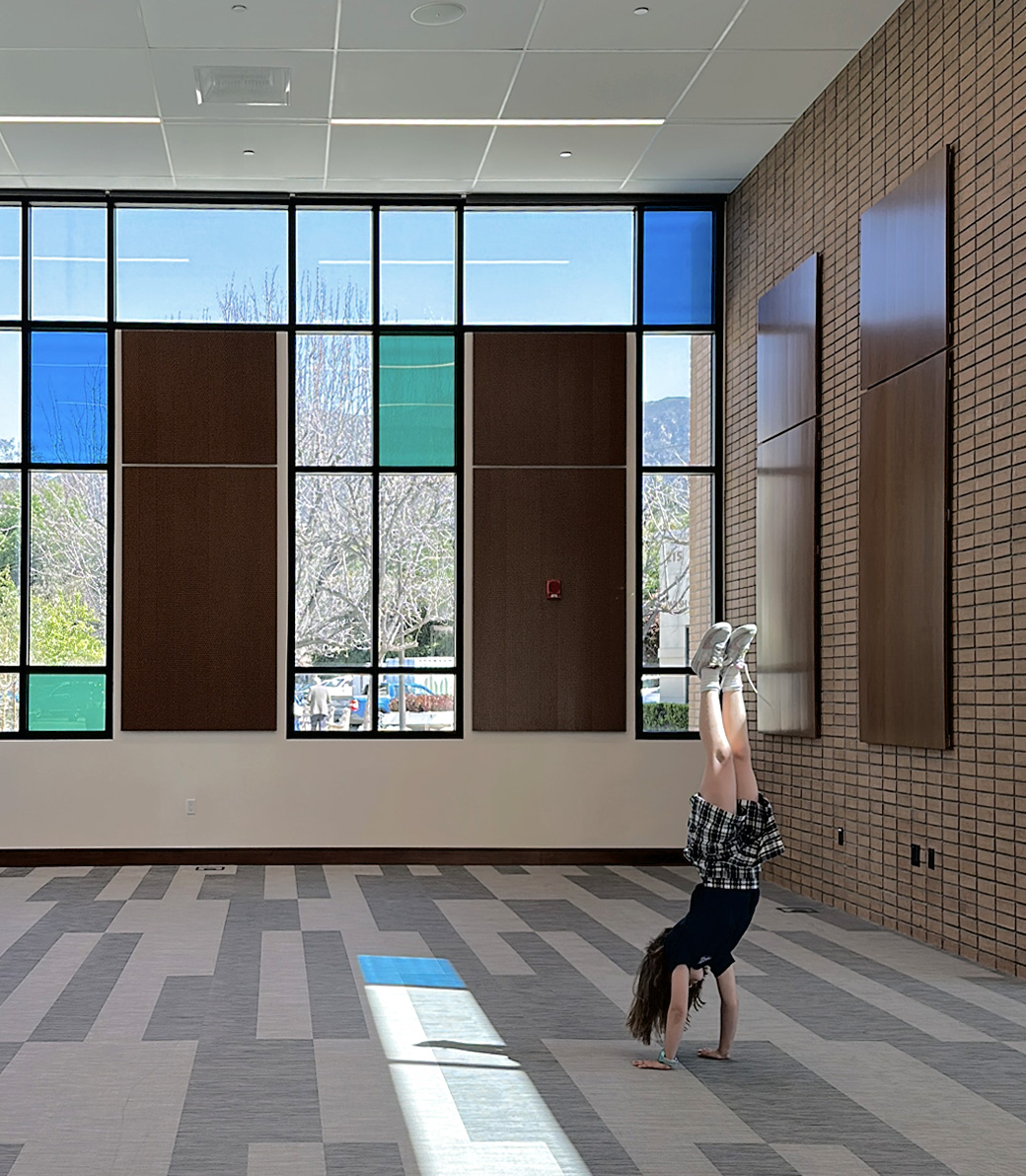 A student does a handstand in front of decorative windows at Saint Bede the Venerable Parish Hall in La Cañada Flintridge, a Pica+Sullivan Southern California religious and educational architectural project.