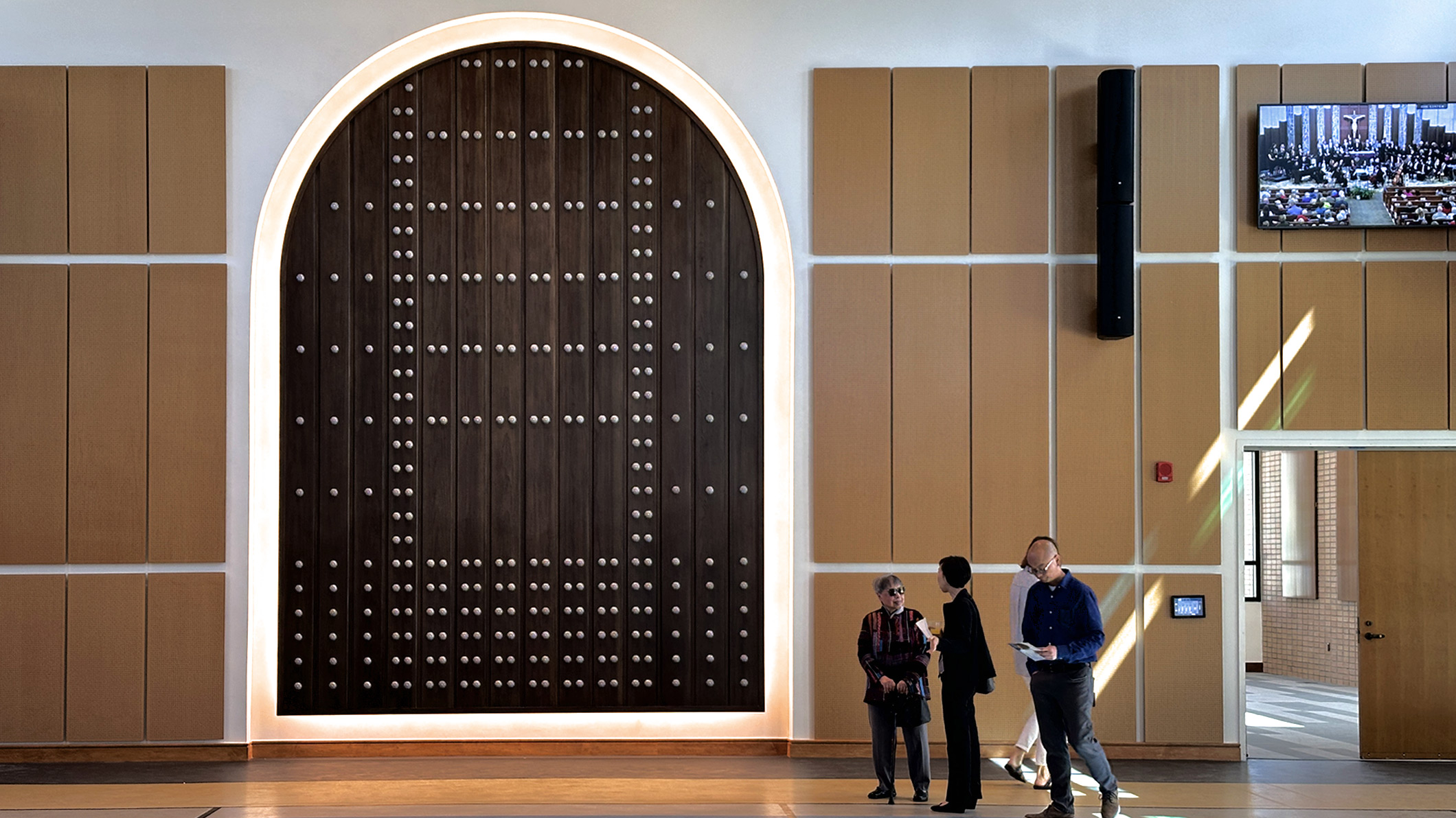 Several people in front of the former church door, now redesigned as a wall decoration honoring the church's history at Saint Bede the Venerable Parish Hall in La Cañada Flintridge, a Pica+Sullivan Southern California religious and educational architectural project.