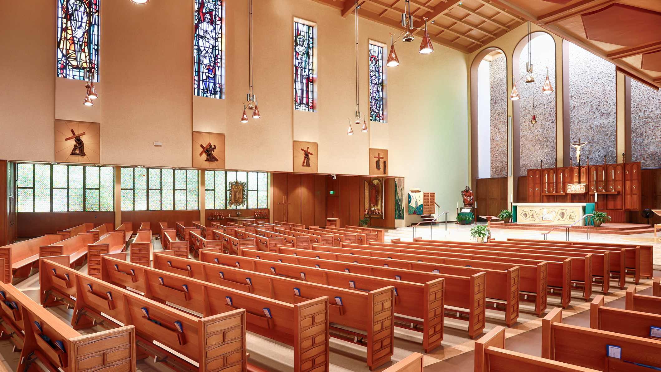 Rows of empty pews sit under stained-glass windows at the Saint Paul the Apostle Church in Los Angeles, a Pica+Sullivan Southern California religious architectural renovation project, facing the altar.